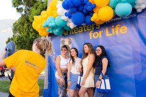 A group of young alumni pose in front of an Anteaters for Life backdrop