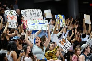 The basketball stadium of fans cheer and hold up signs