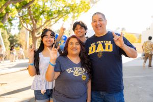 A family of two students with their parents pose and use their hands to zot